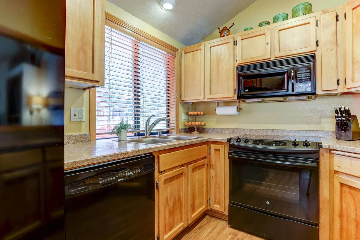 A view into the modern kitchen, with a sink, stove, ample cabinetry, and a window that brings in morning light. The setup invites participation in meal prep and offers a welcoming space for both cooking and socializing.