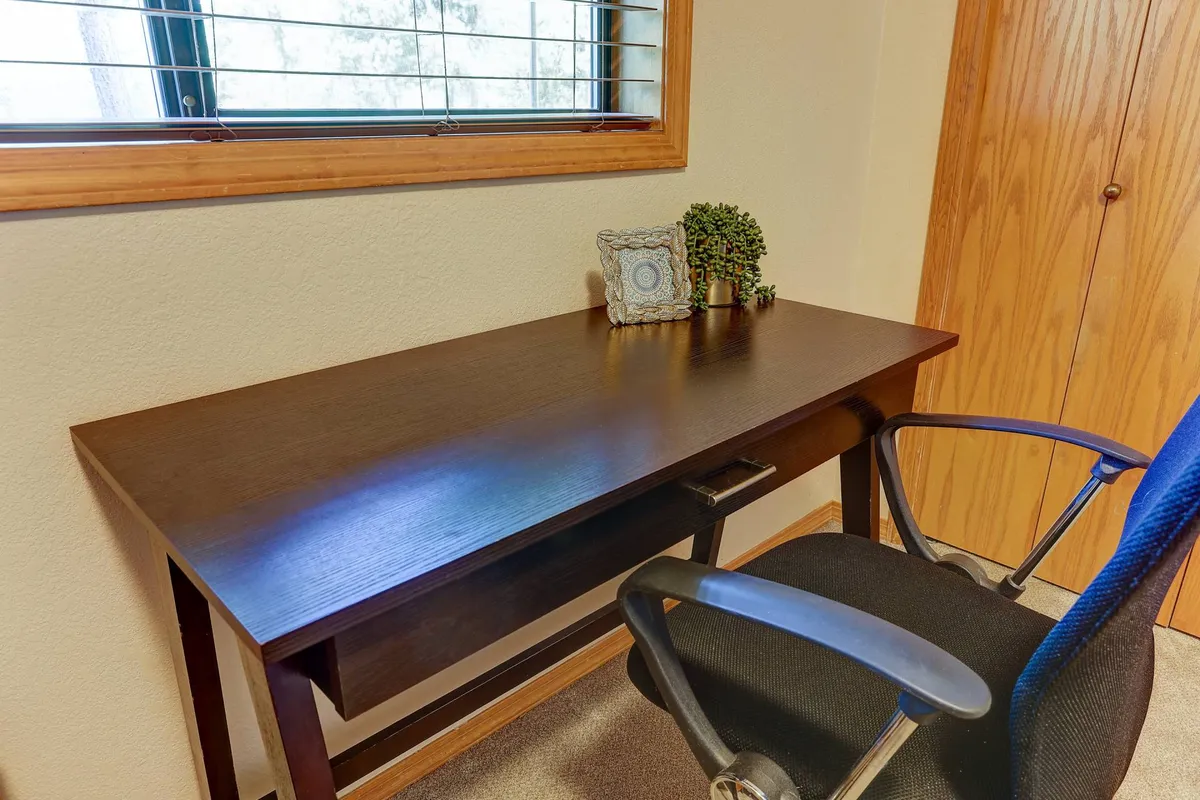 A bright workspace featuring a desk and comfortable chair set beside a window, decorated with tasteful items that create a productive yet welcoming environment. Natural light filters in, making it ideal for working remotely or focusing on creative projects.