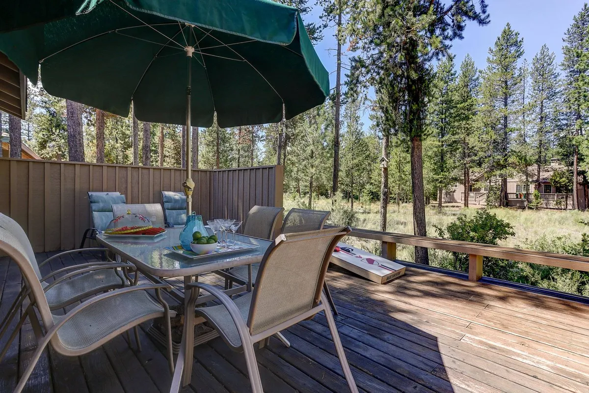 An inviting outdoor dining table with a green umbrella sits on a spacious wooden deck, surrounded by trees—an ideal setting for alfresco dinners, gatherings, and stargazing in the fresh Central Oregon air.