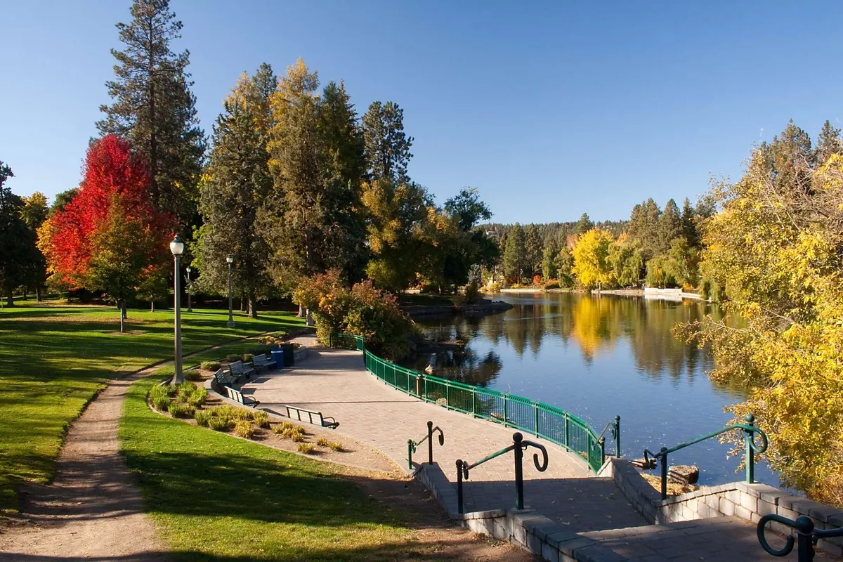 A tranquil outdoor scene with a calm lake bordered by colorful trees and a winding pathway, inviting for walks, cycling, or simply enjoying nature.
