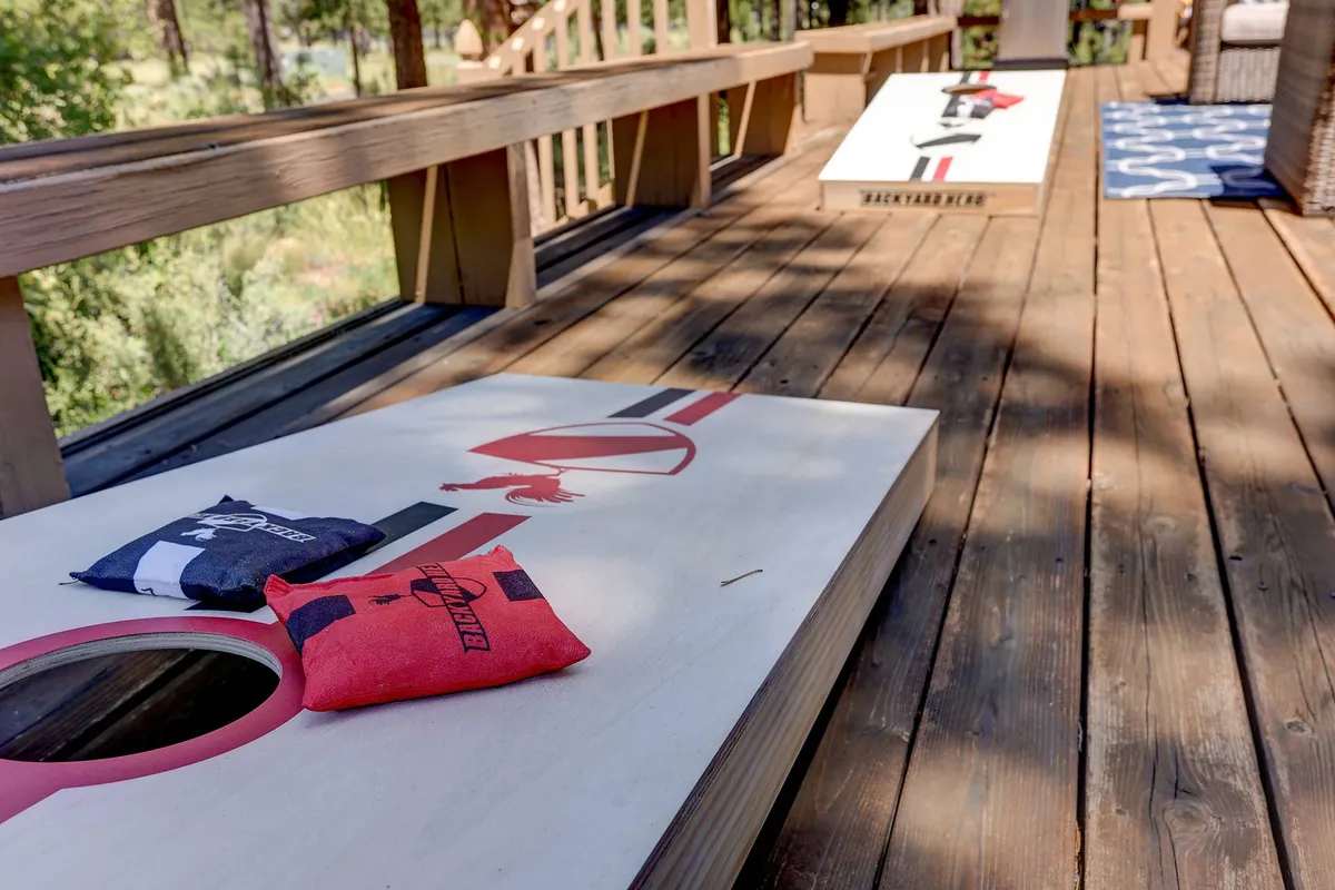 A wooden deck surrounded by greenery, set up for a casual game of cornhole with colorful bean bags and boards. The relaxed, inviting scene hints at both active play and moments of laughter during family gatherings.