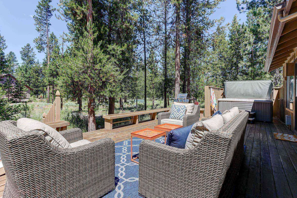 The image showcases the exterior of a classic Sunriver cabin surrounded by towering trees, featuring a cozy outdoor seating area and coffee table—perfect for gatherings. The tranquil natural backdrop sets a peaceful mood, inviting guests to relax, enjoy the outdoors, and experience memorable moments like sunset-watching, stargazing, or hosting a barbecue.