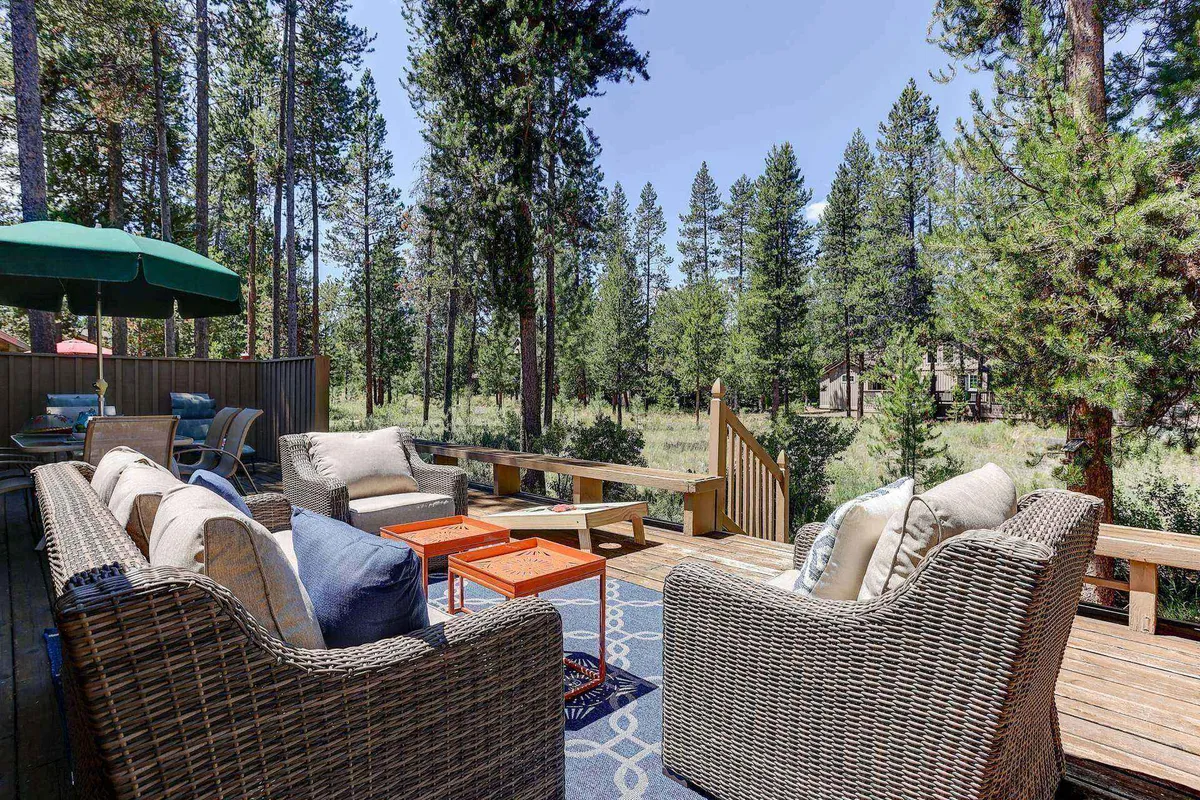A tranquil outdoor seating area featuring comfortable chairs under a green umbrella, set on a wooden deck and surrounded by lush trees. The scene evokes a sense of peaceful relaxation and connection to nature, ideal for enjoying coffee or quiet afternoons outdoors.