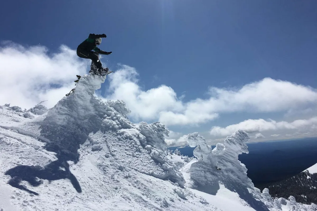 A snowboarder catches air against a backdrop of a snow-covered peak and clear blue sky, capturing the thrill of winter sports at nearby Mt. Bachelor.