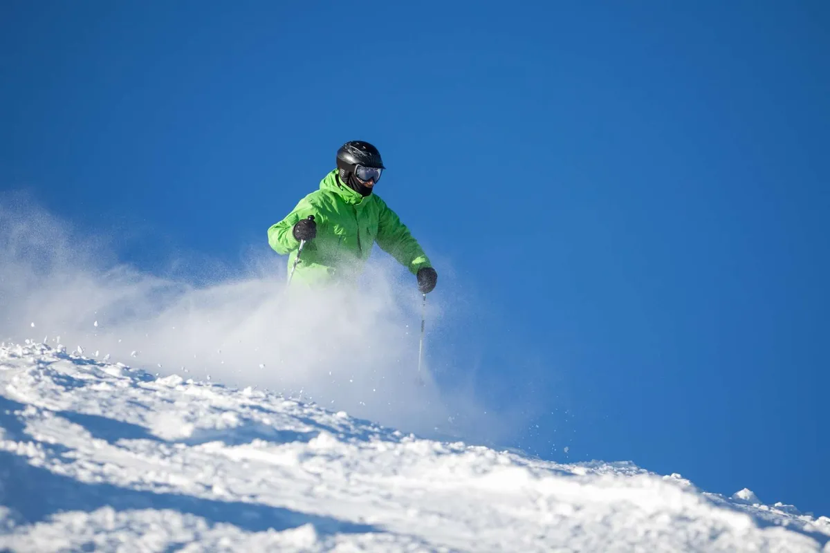 A skier glides down a snow-covered mountain slope beneath a bright blue sky. The snow appears fresh and powdery, capturing the excitement of winter sports and the natural beauty of the surrounding landscape.