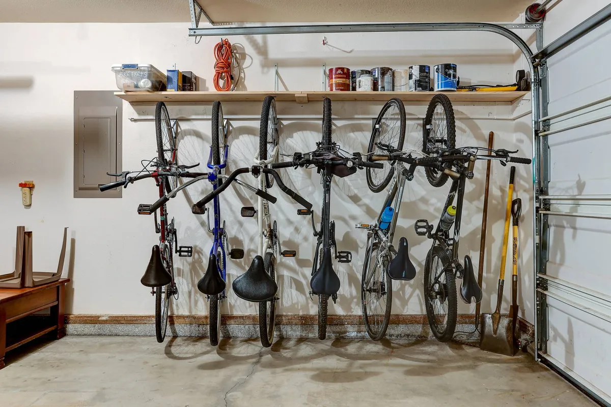 This image features two bicycles hanging on the wall in a neatly organized garage, with shelves stocked with paint cans and tools. Wooden furniture sits in the corner, suggesting a multi-use space for active gear storage and maintenance.